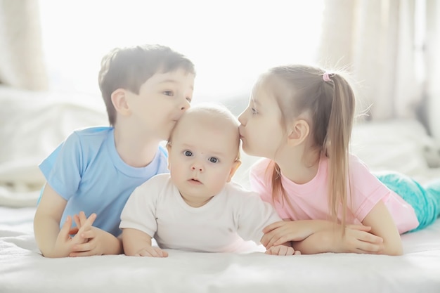 Kinderen liggen op het bed naast de pasgeboren baby, zusje. Emoties van kinderen.