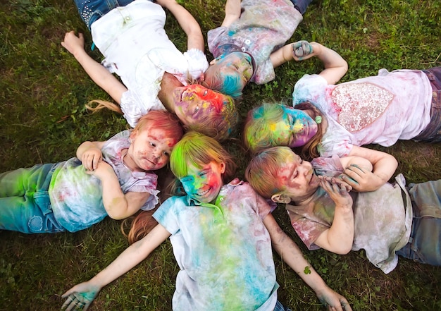 Kinderen liggen op het gras Kinderen geschilderd in de kleuren van het Holi-festival liggen op het gras