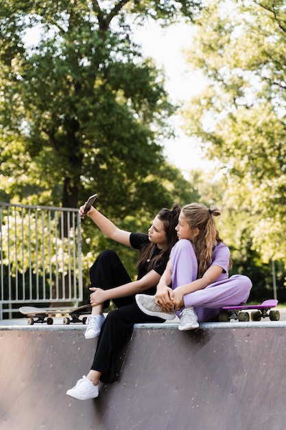 Kinderen meisjes met skateboard en penny boards selfie maken op telefoon op de sport speeltuin kinderen vriendschap concept kinderen vrienden glimlachen en lachen en samen plezier hebben