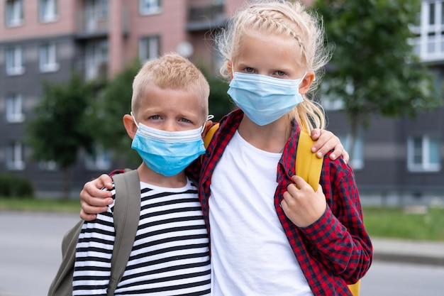 Foto kinderen met een masker en rugzakken beschermen en beschermen tegen het coronavirus voor terug naar school broer en zus gaan naar school nadat de pandemie voorbij is kijkend naar de camera zijn studenten klaar voor het nieuwe schooljaar