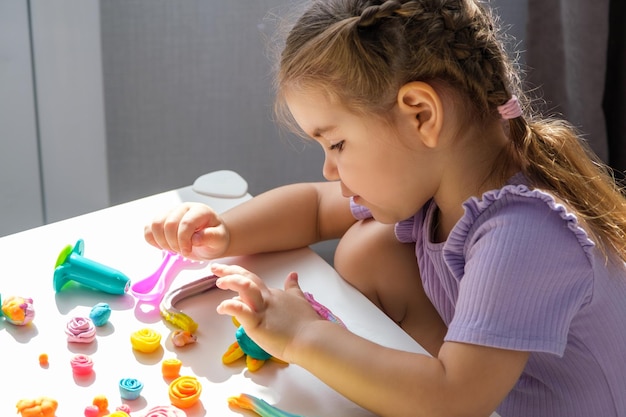 Kinderen met plasticine klein blond meisje beeldhouwt thuis verschillende kleurrijke beeldjes van plasticine