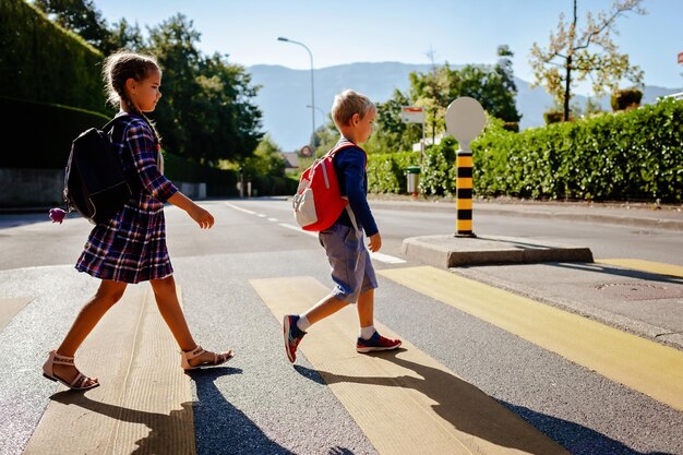 Foto kinderen met rugzakken oversteken de weg bij de voetgangersovergang op weg naar school