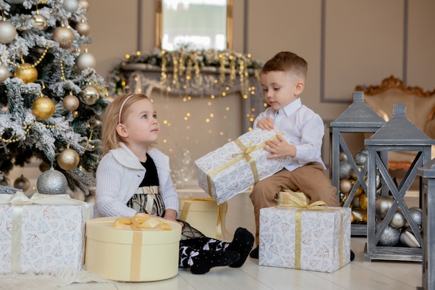 Kinderen onder de kerstboom met geschenkdozen. Ingerichte woonkamer met traditionele open haard