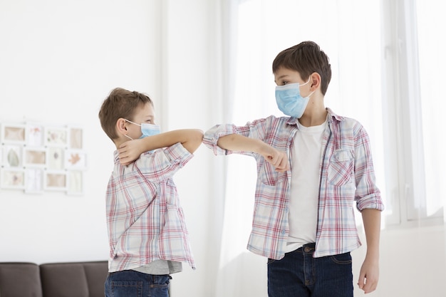 Foto kinderen raken ellebogen terwijl ze binnen zijn en dragen medische maskers