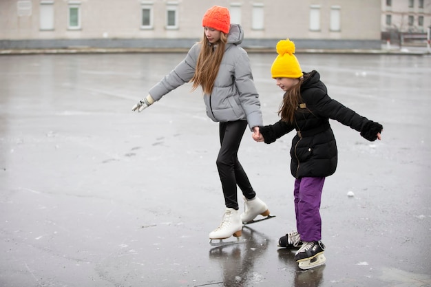 Kinderen schaatsen op de stadsschaatsbaan. De oudere zus leert de jongere schaatsen.