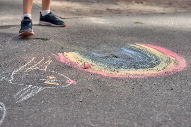 Kinderen schilderen buiten. Portret van een kind dat een regenboog gekleurd krijt trekt op het asfalt op een zonnige zomerdag. Kinderen spelen op de speelplaats. Buiten activiteit