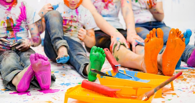 Kinderen schilderen samen met felle kleuren en hun voeten en gezichten zijn bevlekt met verf