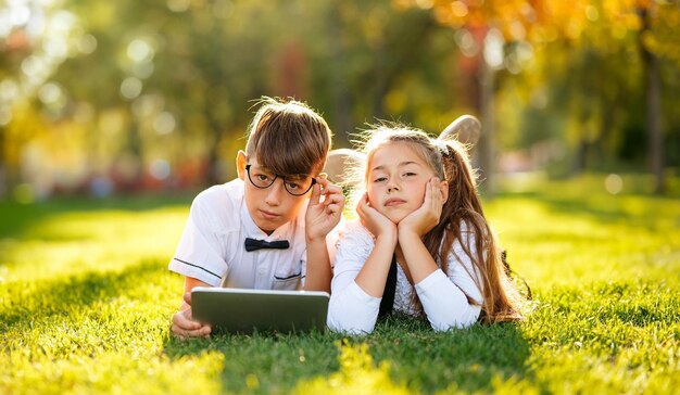 Kinderen schoolkinderen zijn gelukkig in de buurt van de school op het grasveld, rusten tussen de lessen door en leren iets op de tablet