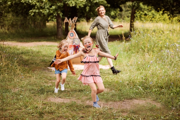 Kinderen spelen buiten met hun moeder. Familie is gekleed in boho-stijl, zussen hebben inheemse amerikaanse make-up op gezichten.