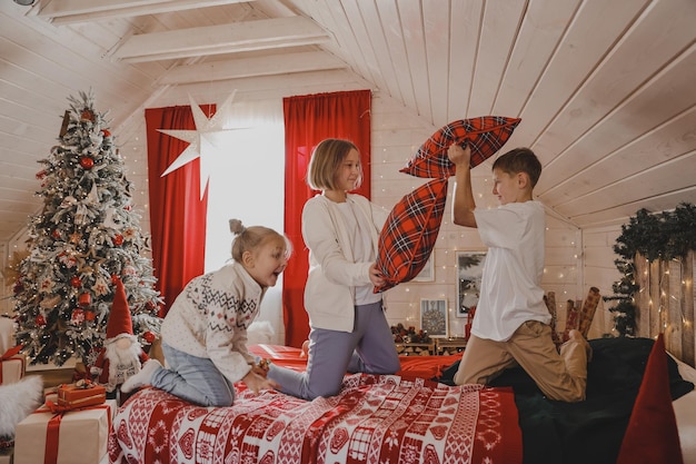 Kinderen spelen met kussens op het bed in de met kerst versierde slaapkamer, kussengevechten, het concept van de nieuwjaarsvakantie