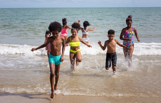 Kinderen spelen rennend op zand op het strand, een groep kinderen hand in hand op een rij op het strand in de zomer, achteraanzicht tegen zee en blauwe lucht