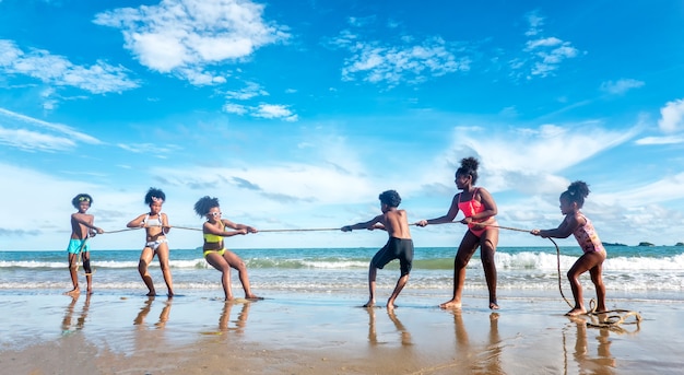 Kinderen spelen rennend op zand op het strand, een groep kinderen hand in hand op een rij op het strand in de zomer, achteraanzicht tegen zee en blauwe lucht