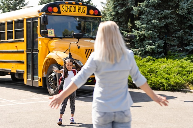 Kinderen student loopt in de handen van moeder om haar te knuffelen na terug naar school in de buurt van de schoolbus