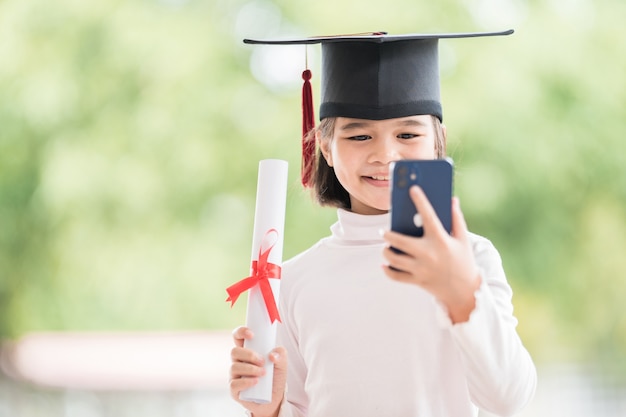 Kinderen studeren af met afstudeerpet en opgerold afstudeercertificaat met smartphone