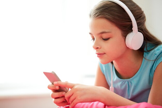 kinderen, technologie en mensen concept - close-up van gelukkig meisje met smartphone en koptelefoon luisteren naar muziek thuis