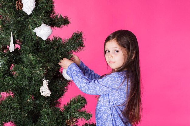 Kinderen vakantie en kerst concept meisje versieren kerstboom op roze achtergrond