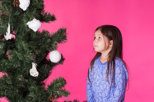 Kinderen vakantie en kerst concept meisje versieren kerstboom op roze achtergrond