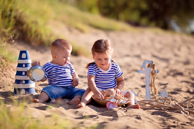 Kinderen verkleed als matrozen op een zandstrand met schelpen aan zee