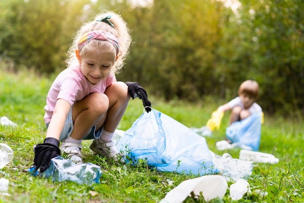 Kinderen verwijderen plastic afval en stoppen het in een biologisch afbreekbare vuilniszak in de open lucht. Het concept van ecologie, afvalverwerking en natuurbescherming. Milieubescherming.