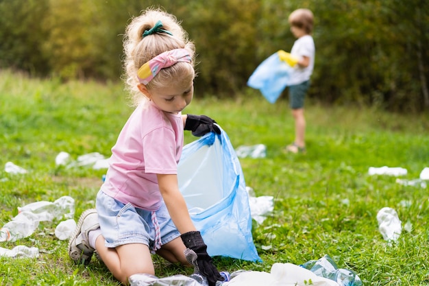 Kinderen verwijderen plastic afval en stoppen het in een biologisch afbreekbare vuilniszak in de open lucht. Het concept van ecologie, afvalverwerking en natuurbescherming. Milieubescherming.