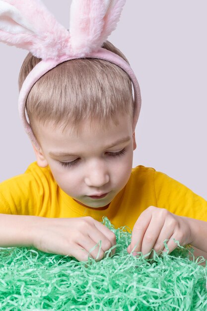 Kinderen vieren Pasen Een grappig kind met konijnenoren zoekt paaseieren in groen papier dat gras imiteert