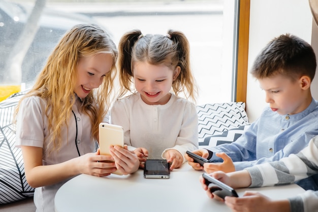Kinderen zitten aan een tafel in een café en spelen samen mobiele telefoons. Modern amusement.