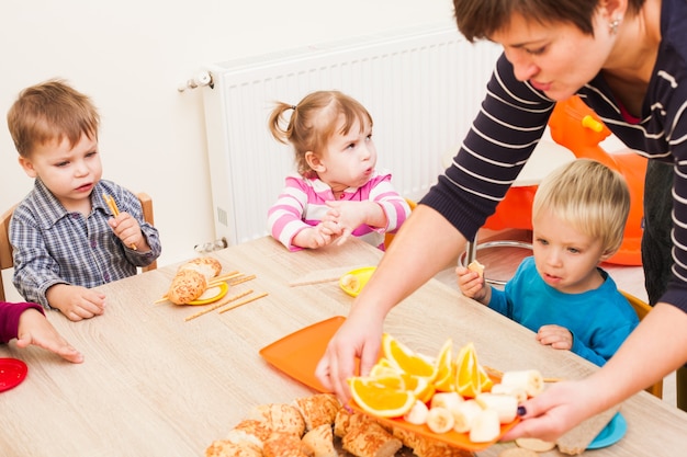 Kinderen zitten aan tafel met lunch en eten fruit en gebak