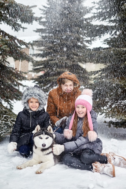 Kinderen zitten in de sneeuw en streelden hond husky. Kinderen gaan in de winter uit met husky's