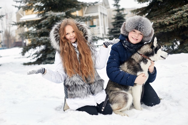 Kinderen zitten in de sneeuw en streelden hond husky