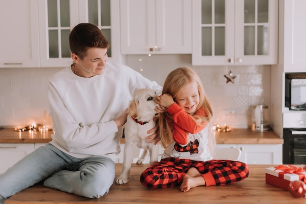 Kinderen zitten met hun geliefde hond in de kerstkeuken. familie tijdverdrijf. levensstijl. broer en zus, jongen en meisje spelen en dollen met een huisdier. ruimte voor tekst. Hoge kwaliteit foto