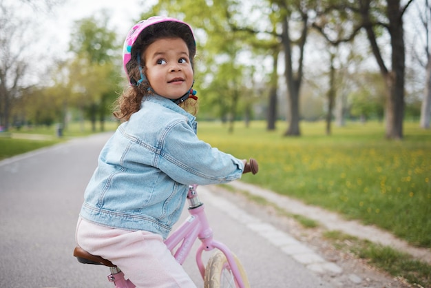 Kinderfiets en leren rijden met een meisje in het park op haar fiets terwijl ze een helm draagt voor de veiligheid buiten Zomer fietsen en kinderen met een gelukkig vrouwelijk kind trainen om te fietsen in een tuin