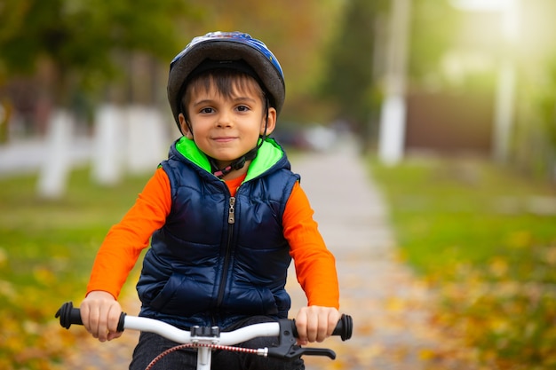 헬멧을 쓰고 가을 날 자전거를 타는 유치원 소년. 활동적인 건강한 야외 스포츠. 빈 공간이있는 사진.