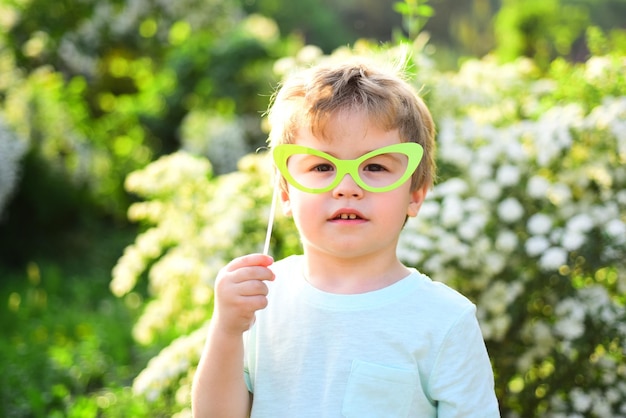 Kindergeluk Kinderdag lentevakantie Zonnig weer Gelukkig kind in de bloeiende natuur Klein jongenskind in groen bos Klein kind met zomerfeestbril Positieve uitdrukken