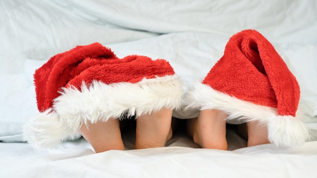 Kinderhakken liggen op het bed onder een witte deken in hoedenkappen van de kerstman Het concept van Kerstmis een fijne vakantie