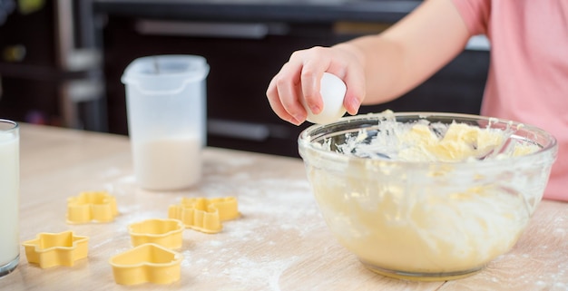 kinderhand breekt een ei in een kom koekjesdeeg