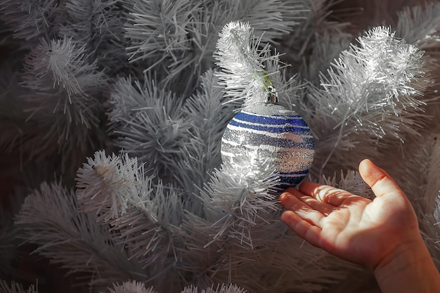 kinderhand hangt kerstspeelgoed aan een kunstmatige witte kerstboom