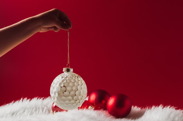 Kinderhand houdt een kerstversiering van een glazen bol vast tegen een witte zachte wollen deken