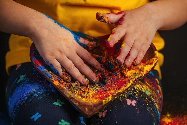 kinderhanden die een bord vasthouden in de vorm van een hart met kleurrijke Holi-kleuren