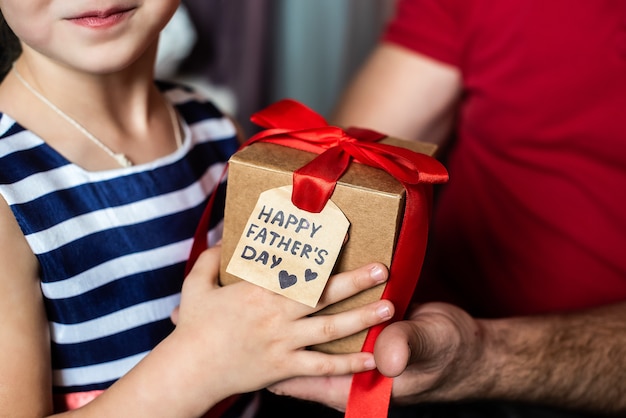 Kinderhanden geven een doos met een rode strik en een ansichtkaart