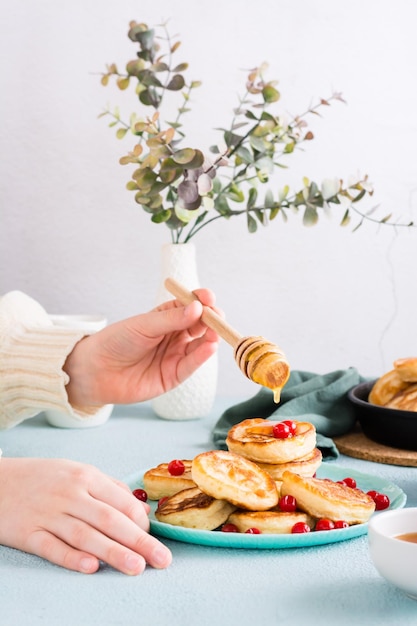 Kinderhanden gieten honing over pannenkoeken en veenbessen op een bord Zelfgemaakt ontbijtdessert Verticale weergave