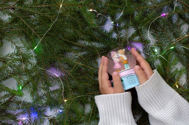 Foto kinderhanden houden een stuk speelgoed vast tegen de achtergrond van kerstboomtakken. het concept van nieuwjaar en kerstmis zonder afval.