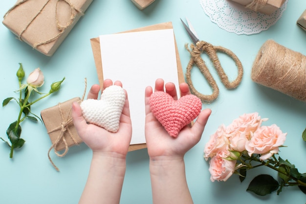 Kinderhanden houden twee gebreide harten vast op de achtergrond van een vintage compositie voor Valentijnsdag