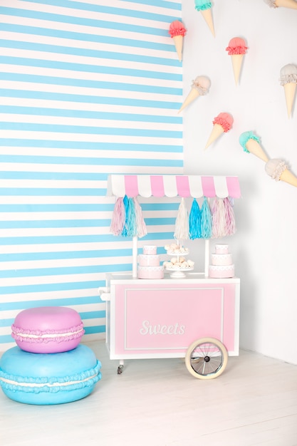 Kinderkamer met blauwe streep. candy stall fotozone met grote bitterkoekjes, snoep en marshmallows. trolley met ijs. Kamer ingericht voor verjaardag. Winkelwagen met Candy Bar.