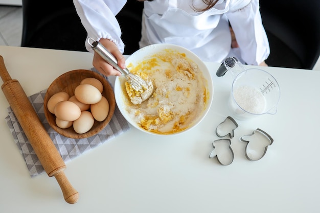 Kinderkok roert deeg voor koekjes met een garde