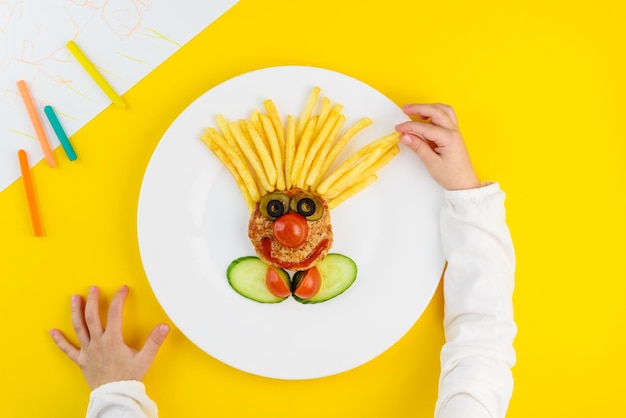Kinderlunch in de vorm van een clownkotelet frites tomaat komkommer met kinderhandjes