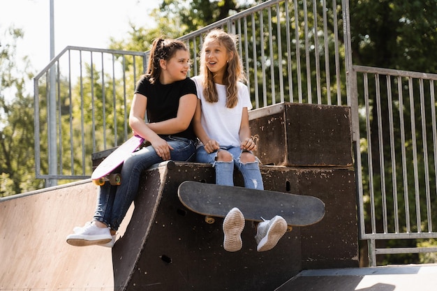 Kindermeisjes glimlachen en lachen en hebben samen plezier Kinderen met skateboard en pennyboards communiceren en discussiëren op de sportspeeltuin Meisjes vriendschapsconcept