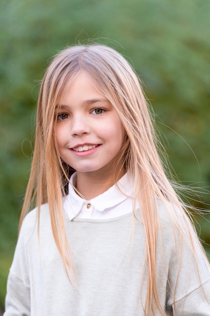 Kindermode en stijl. Schoonheid, jeugd, groei. Gelukkig kindertijdconcept. Meisje met blonde lange haarglimlach op natuurlijk landschap. Kind in grijze trui op idyllische herfstdag.