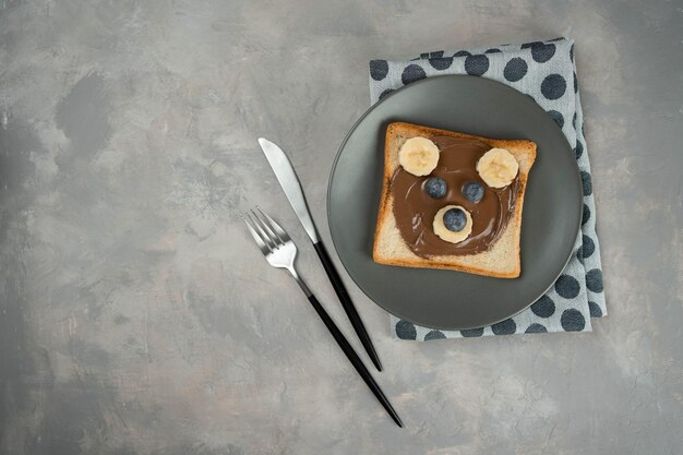 Kinderontbijt of lunch of snacktoast met chocolade-hazelnootpasta, banaan en bosbes in de vorm van een schattig beertje. Kindermenu menu