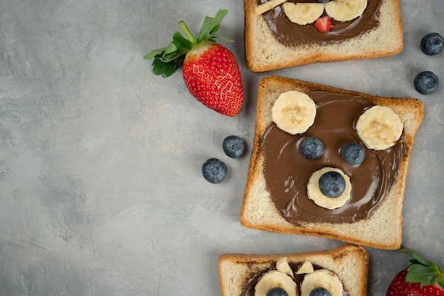 Kinderontbijt of lunch of snacktoast met chocolade-hazelnootpasta, banaan en bosbes in de vorm van een schattig beertje. Kindermenu menu