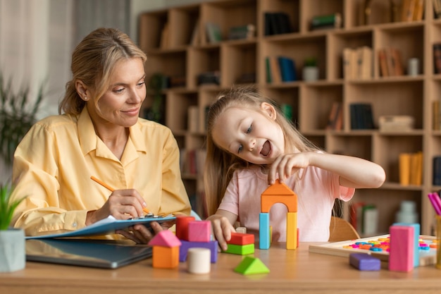 Kinderpsychologie-examen Klein meisje speelt met kleurrijke houten blokken professionele kinderpsycholoog die notities schrijft